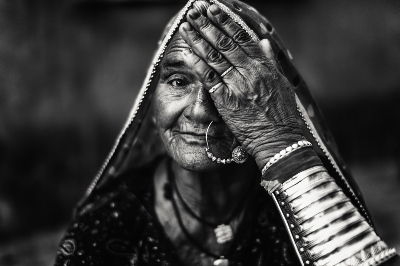 An elderly Rajasthani woman shades one eye beneath a printed veil in Pushkar — fine art black-and-white portrait by Sefa Yamak, India series.