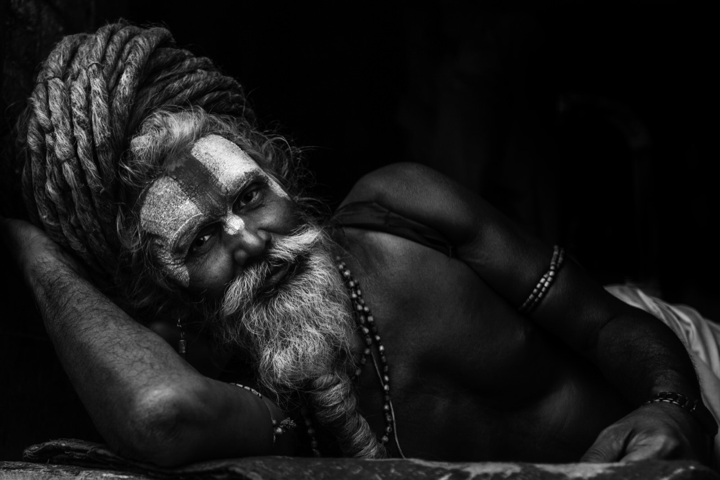 A reclining sadhu with coiled dreadlocks and white Vaishnavite forehead paint in Varanasi — fine art black-and-white portrait by Sefa Yamak, India series.