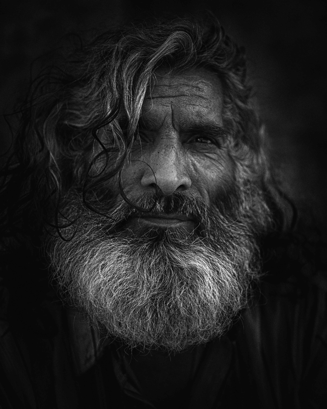 Uzun dalgalı saçlı ve gür gri sakallı bir adam derin gölgenin içinden çıkıp kameraya bakıyor — Sefa Yamak'tan sokak fotoğrafı, İstanbul serisi.