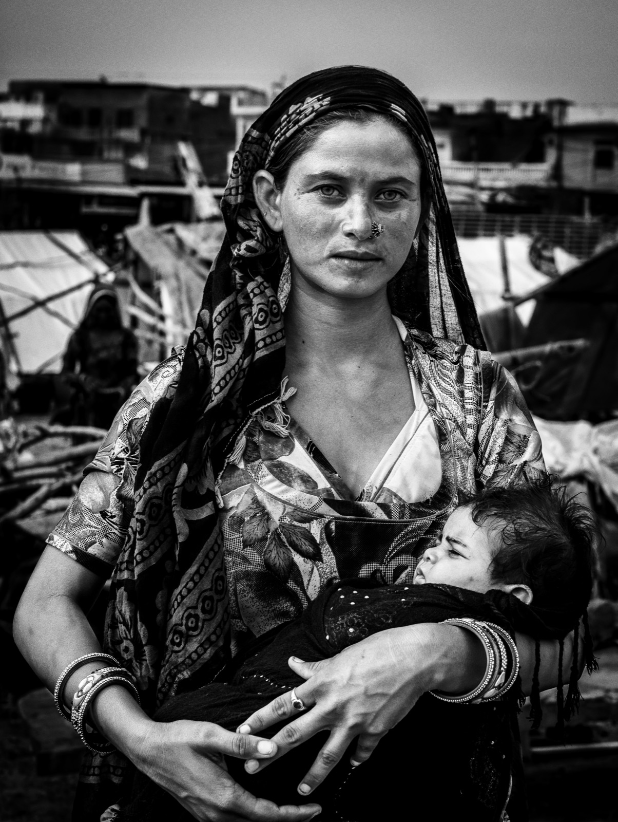 A young Roma mother holds her sleeping baby at the Pushkar fairground — fine art black-and-white portrait by Sefa Yamak, India series.