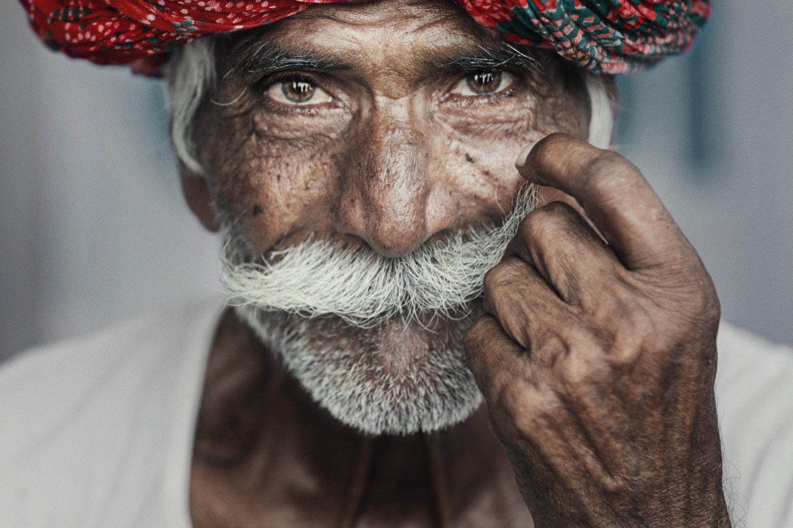 An old man in a red Rajasthani turban twists his white moustache in Pushkar — fine art colour portrait by Sefa Yamak, India series.