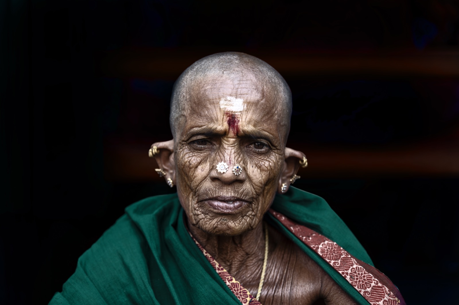 An elderly woman with a shaved head and green sari at a temple in southern India — fine art colour portrait by Sefa Yamak, India series.