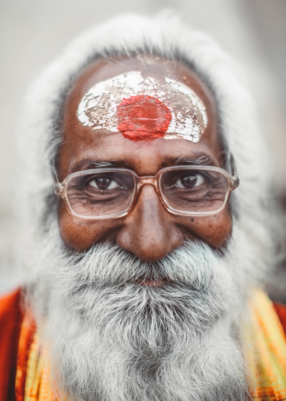 Close-up of a bespectacled sadhu with cracked white-and-red forehead paint by the Ganges in Varanasi — fine art portrait by Sefa Yamak, Sadhus series.