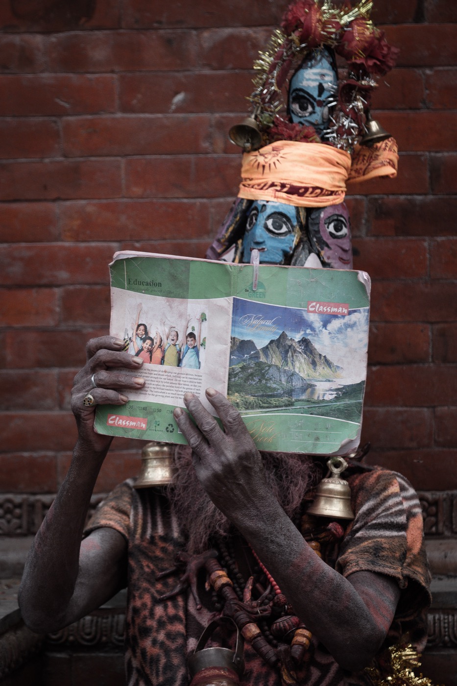 An Aghori sadhu reads a child's notebook before a blue Kali idol in Varanasi — fine art colour portrait by Sefa Yamak, Sadhus series.