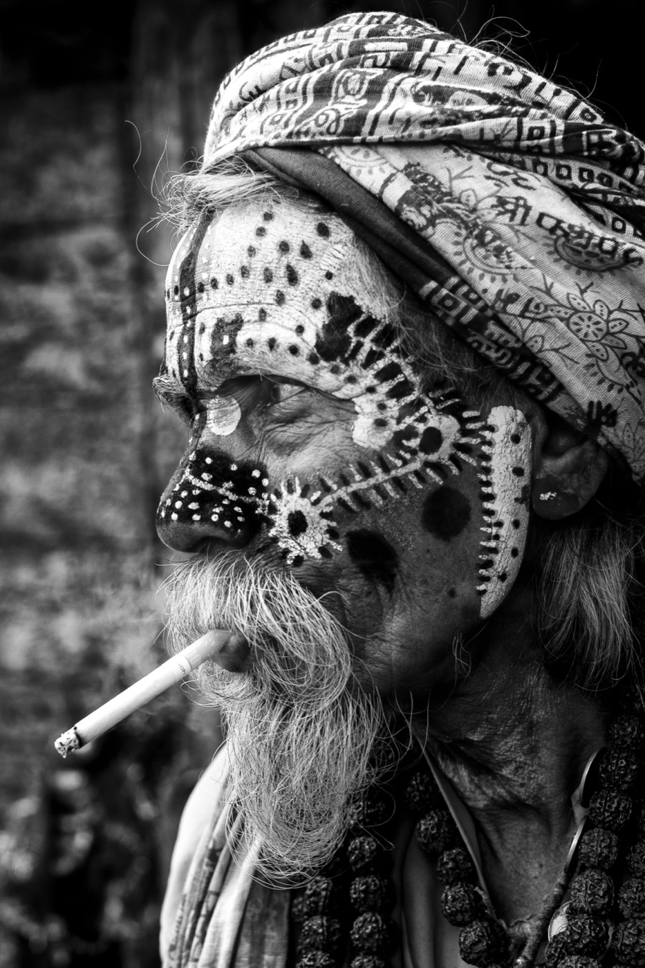 Profile of a sadhu with intricate white dot face paint and a cigarette, Varanasi — fine art black-and-white portrait by Sefa Yamak, Sadhus series.