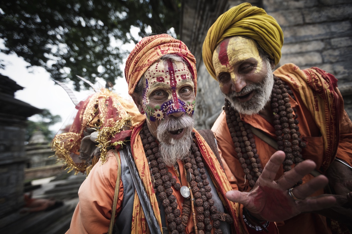 Two laughing sadhus in festival face paint greet the camera outside a temple in Varanasi — fine art colour portrait by Sefa Yamak, Sadhus series.