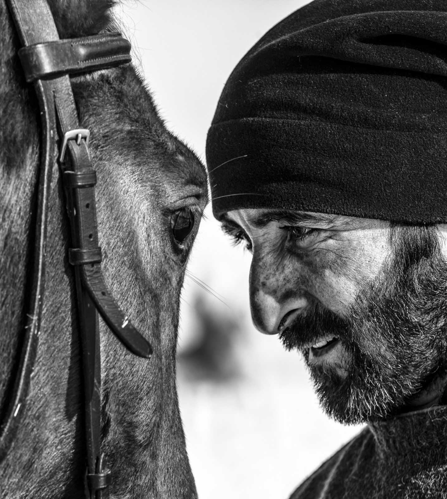 Yün başlıklı sakallı bir adam alnını bir atın alnına dayamış, kışın göz göze — Sefa Yamak'tan güzel sanatlar siyah-beyaz portre, En Zorlu Kış serisi.
