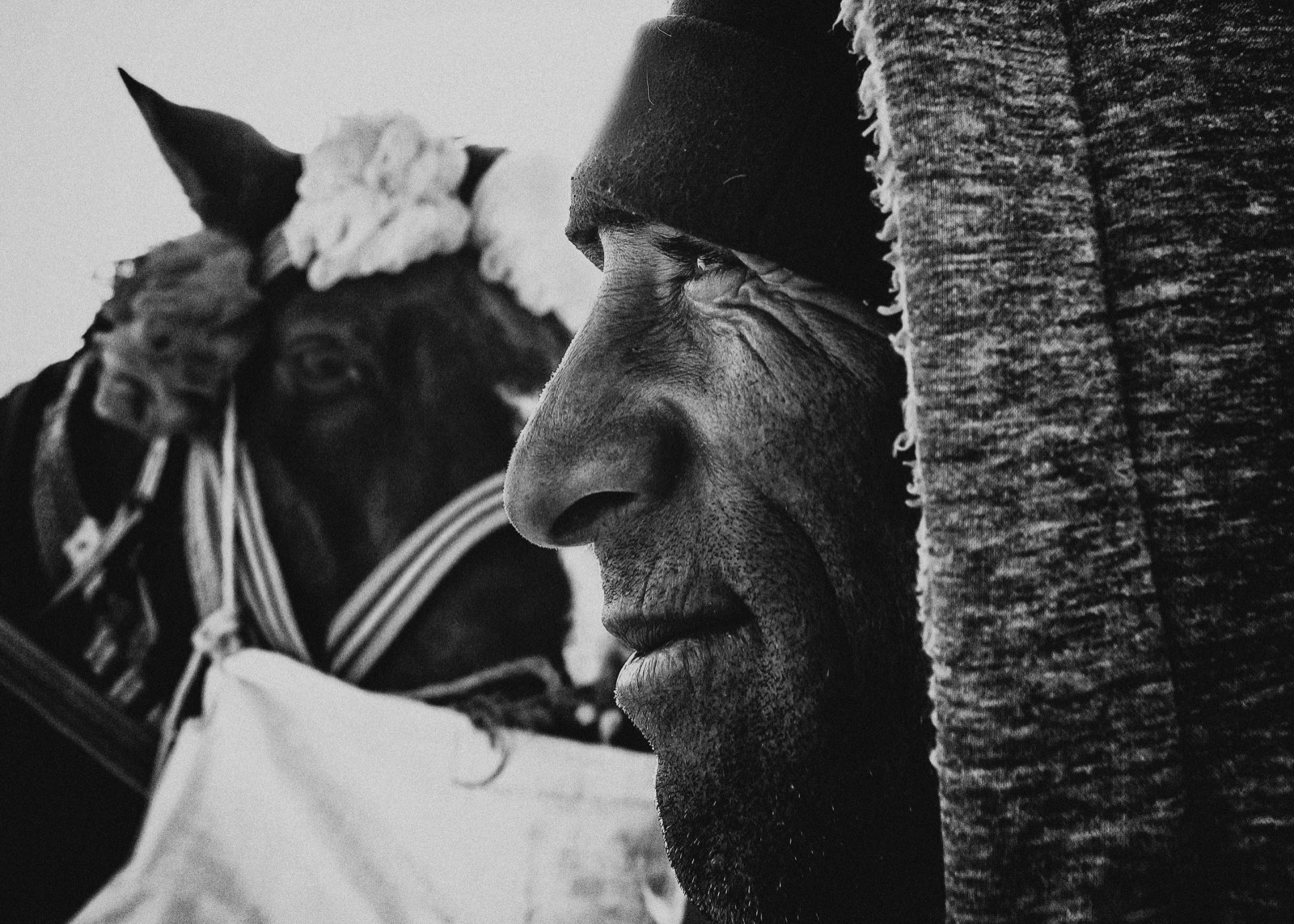 Yıpranmış bir adamın, kış oyunundan önce süslü atının yanındaki siyah-beyaz profili — Sefa Yamak'tan güzel sanatlar portre, En Zorlu Kış serisi.